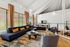 Spacious living room with a black sectional sofa, vibrant orange cushions, and large windows with drapes.