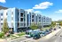 Modern four-story apartment building with blue facade located on a bustling city street.