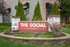 Charming entry sign of The Social on Hovey surrounded by lush greenery and vibrant flowers.