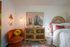 Inviting bedroom featuring a plush orange chair, a wicker cabinet, vibrant decor, and a cozy bed with textured bedding.