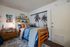 Cozy bedroom with stylish decor, featuring a wooden bed, vibrant cushions, and tropical wall art.