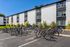 Contemporary apartment building with bicycle racks and green landscaping under a clear blue sky.