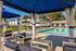 Inviting outdoor pool area with modern lounge seating under blue canopies, surrounded by lush greenery.
