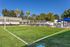 Inviting outdoor area with a grass volleyball court, shaded picnic tables, and cozy cabanas under a clear blue sky.