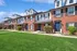 Row of brick townhouses with blue doors and lush green lawns under a sunny blue sky.