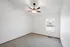 Spacious bedroom with plush carpeting and a ceiling fan, featuring a large window for natural light.
