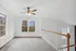 Sunlit loft area with carpeted floor, large windows, and a ceiling fan.