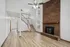 Spacious living area with a rustic brick fireplace, wooden flooring, and a stylish staircase.