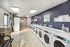 Bright and modern laundry room with multiple washing and drying machines along a tiled path.