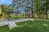 Lush outdoor patio with pergola, picnic table, and barbecue grill surrounded by greenery and trees.