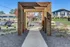 Inviting wooden arch frames a scenic walkway with landscaped gardens and parking, leading to residential buildings.