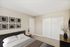 Modern bedroom with minimalist decor, featuring a cozy bed, framed artwork, and sliding closet doors.