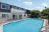 Inviting outdoor pool area adjacent to modern apartment building, surrounded by lush greenery and clear skies.
