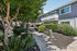 Charming apartment complex with lush greenery, benches, and well-maintained pathways under a clear blue sky.