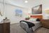 Modern bedroom with stylish decor, featuring an orange headboard, cozy bed, artwork, and natural light.