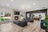 Spacious open-concept living room with elegant black sofas, a fireplace, modern lighting, and a sleek kitchen with bar seating.
