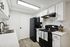 Modern kitchen with sleek black appliances, white cabinets, and wood flooring.