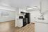 Sleek kitchen with white cabinets, black appliances, and wood flooring in a spacious open area.