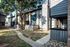 Charming two-story apartment building with a wood and brick facade, surrounded by lush greenery and a paved walkway.