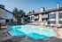 Inviting outdoor pool with lounge chairs and apartments in the background, set under clear blue skies.