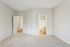 Bright and inviting bedroom with plush carpet, featuring a view into a modern bathroom and hallway with warm wood flooring.