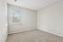 Bright and spacious carpeted bedroom with large windows, neutral walls, and ample natural light.