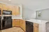 Modern kitchen featuring sleek black appliances, elegant wooden cabinetry, and a spacious white countertop with dual sink, flowing into an inviting open living area with natural light.