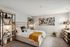 Cozy and stylish bedroom with modern decor, featuring a plush bed adorned with decorative pillows and a warm throw, complemented by sleek shelving and elegant artwork on the wall.