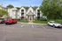 Charming apartment complex with inviting entrance, surrounded by lush greenery, offering abundant parking and a serene living environment.