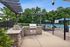 Charming outdoor area featuring a modern stone barbecue grill under a stylish pergola with inviting views of the sparkling pool and lush greenery.