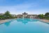 Luxurious apartment complex showcasing a pristine swimming pool with lounge chairs and blue umbrellas, surrounded by lush greenery and modern architecture under a clear sky.