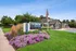 Inviting entrance of Renew Belcamp Apartment Homes, featuring a beautifully landscaped garden with vibrant flowers, modern signage, and an American flag for a welcoming atmosphere.