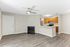 Modern open-concept living area with elegant gray wood flooring, a cozy fireplace, and sleek kitchen featuring stainless steel appliances and stylish cabinetry.