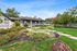 Charming single-story home with a spacious porch and vibrant landscaped garden, set against a clear blue sky.