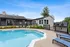 Inviting outdoor pool area with elegant lounge chairs and charming clubhouse surrounded by lush greenery under a clear blue sky.