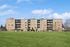 Charming apartment building with spacious balconies and lush green surroundings under a vibrant blue sky.