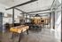 Modern communal space with sleek industrial design, featuring a polished concrete floor, stylish seating, and a vibrant foosball table.