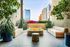 Chic urban patio featuring lush greenery, modern benches, and a cozy fire pit with cityscape views.