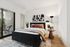 Bright and airy bedroom with modern decor, featuring a cozy bed, stylish artwork, and access to a serene balcony through sliding glass doors.