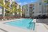 Luxurious apartment complex featuring a sparkling pool, surrounded by modern architecture and lush palm trees.