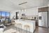 Modern apartment interior featuring a sleek kitchen with stainless steel appliances, white cabinetry, and an inviting island with bar stools, complemented by a bright living area with large windows and stylish decor.