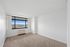 Bright and spacious room with large window offering stunning city views, featuring plush carpet and neutral walls.