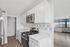 Modern kitchen with sleek white cabinetry and stainless steel appliances opening into a bright, spacious living area with large windows.