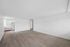 Spacious open-plan apartment with elegant wood flooring, bright white walls, and modern kitchen in the background.