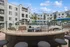 Elegant apartment courtyard featuring a chic bar area with granite countertop, stylish seating, sparkling pool, and lush palm trees under a clear sky.