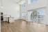 Bright and modern living space featuring high ceilings, large windows, and sleek hardwood floors, seamlessly connected to a contemporary kitchen with stylish cabinetry.