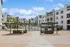Elegant apartment complex courtyard featuring modern pergolas, lush palm trees, and stylish outdoor seating against a backdrop of pristine white architecture and a vibrant blue sky.
