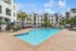 Luxurious apartment community with a stunning outdoor pool, surrounded by elegant white buildings and tropical palm trees.