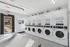 Modern and bright laundry room featuring multiple stacked washers and dryers, with sleek stainless steel folding tables and outdoor access.