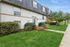 Charming apartment exterior with lush landscaping, vibrant pink flowers, and inviting greenery, under a clear blue sky.